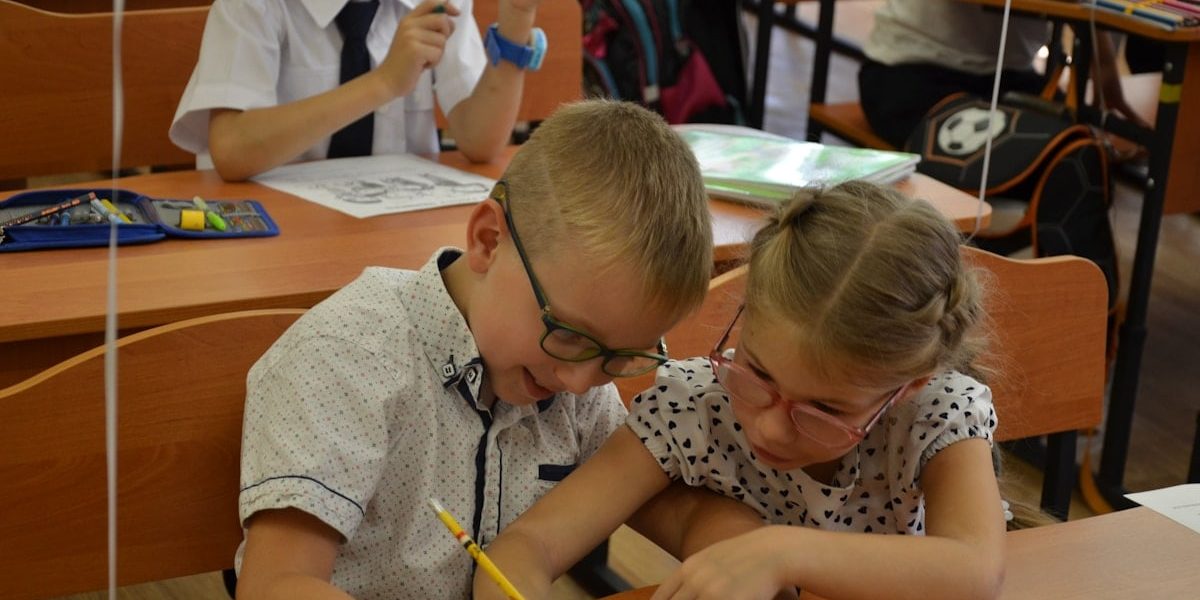 Two diverse elementary school children classmates studying together at desk